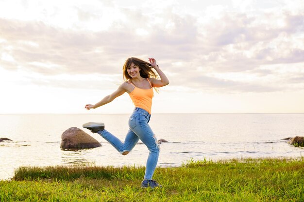 Junges Mädchen mit langen Haaren in Jeans und gelbem T-Shirt springt auf einen wunderschönen Sonnenuntergang vor dem ...