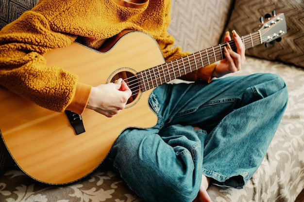 Junges Mädchen mit langen Nägeln spielt zu Hause Akustikgitarre Teenager sitzt auf der Couch im Zimmer und lernt Gitarre zu spielen