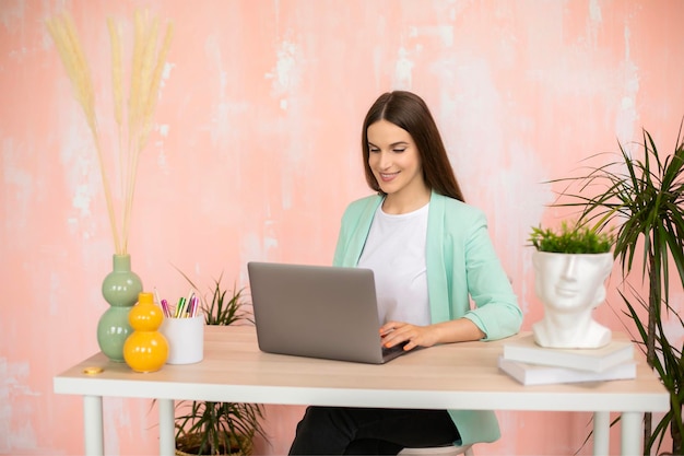 Junges Mädchen mit Laptop-Computer, das in einem farbenfrohen Büro sitzt und auf den Bildschirm schaut