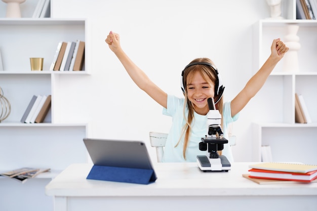 Junges Mädchen mit Mikroskop während der Online-Unterrichtsausbildung zu Hause