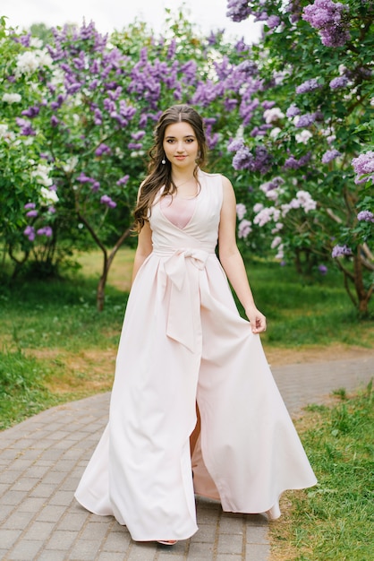 Junges Mädchen mit professionellem Make-up plus Größe in einem blühenden lila Garten in einem schönen langen rosa Kleid