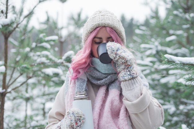 Junges Mädchen mit rosa Haaren, die Tee im Winterwald trinken