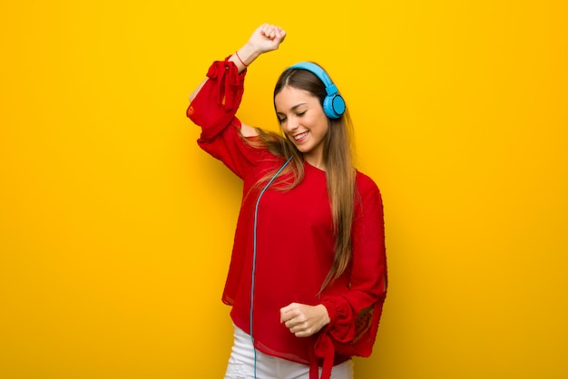 Junges Mädchen mit rotem Kleid über gelber Wand hörend Musik mit Kopfhörern und Tanzen