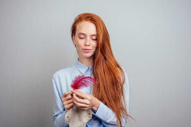 Foto junges mädchen mit roter feder auf grauem hintergrund