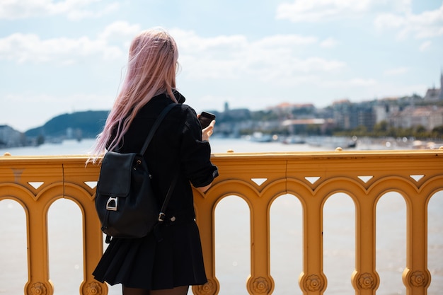 Junges Mädchen mit Rucksack und rosa Haaren, machen Sie ein Foto mit Smartphone von der Brücke.