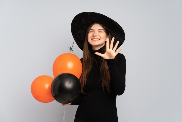 Junges Mädchen mit schwarzem Hut und schwarzem Kleid, das Ballons hält