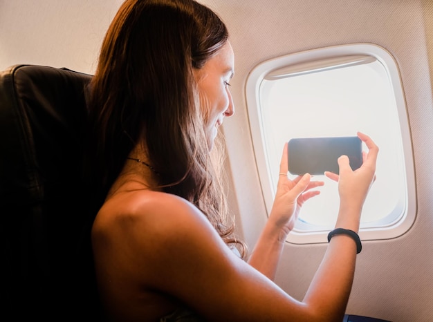 Junges Mädchen mit Smartphone und Blick durch das Fenster im Flugzeug