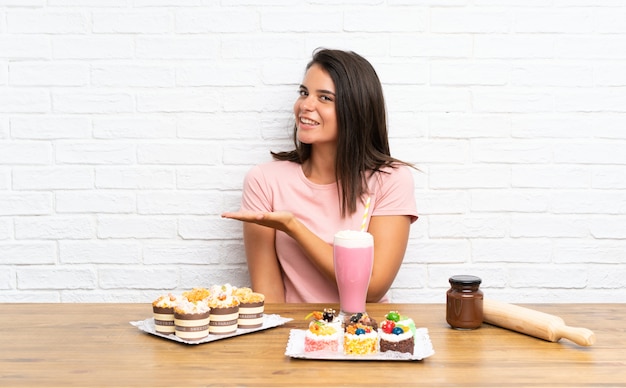 Junges Mädchen mit vielen verschiedenen Minikuchen, die Hände zur Seite für die Einladung ausdehnen, um zu kommen