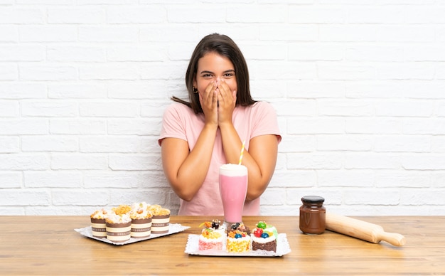 Junges Mädchen mit vielen verschiedenen Minikuchen mit Überraschungsgesichtsausdruck