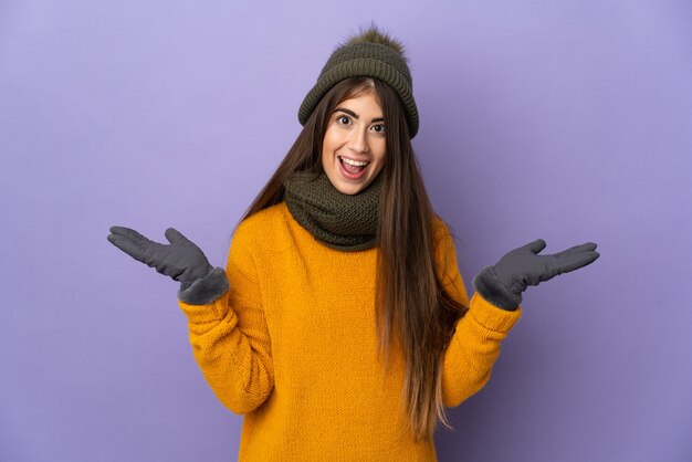 Junges Mädchen mit Wintermütze lokalisiert auf lila Wand mit schockiertem Gesichtsausdruck