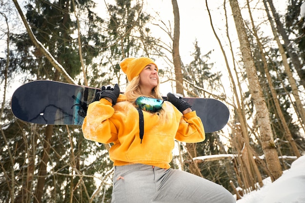 Junges Mädchen oder Snowboarderin macht Wintersport im verschneiten Wald, sie steht im Schnee und hält ein Snowboard
