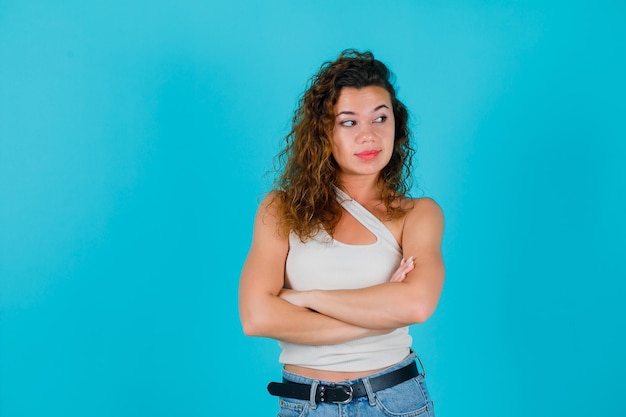 Junges Mädchen schaut nach rechts, indem es die Arme auf blauem Hintergrund kreuzt