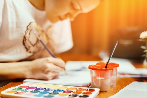 Junges Mädchen sitzt am Tisch in ihrem Zimmer und malt mit Aquarellfarben Thema Kreativität, Inspiration und Zeichnung