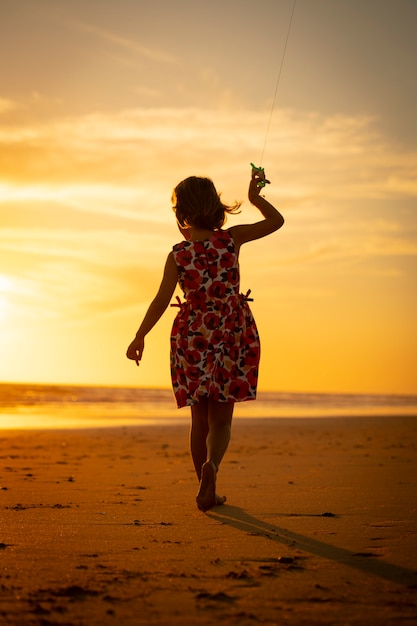 junges Mädchen spielt mit Drachen am Strand bei Sonnenuntergang