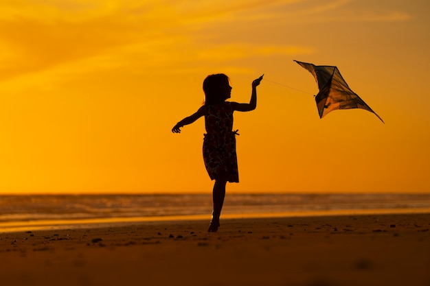 junges Mädchen spielt mit Drachen am Strand bei Sonnenuntergang