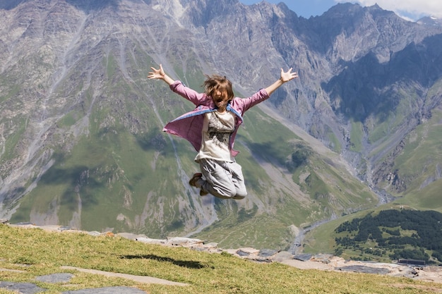 Junges Mädchen springt mit erhobenen Händen und schreit gegen den Himmel und die Berge