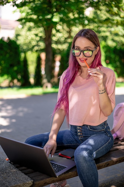 Junges Mädchen studiert im Frühlingspark, sitzt auf der Holzbank und surft auf ihrem Laptop