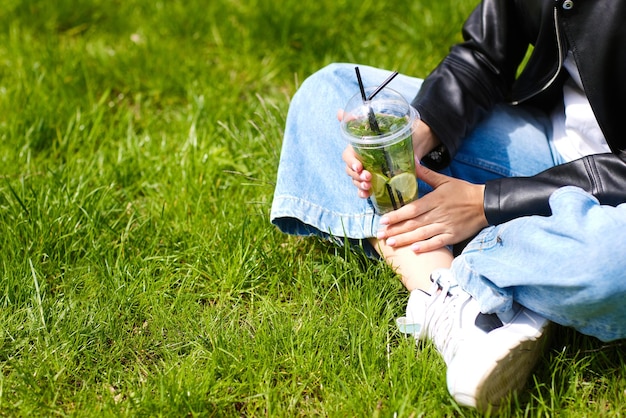 Junges Mädchen trinkt einen erfrischenden Cocktail mit Eis auf grünem Gras