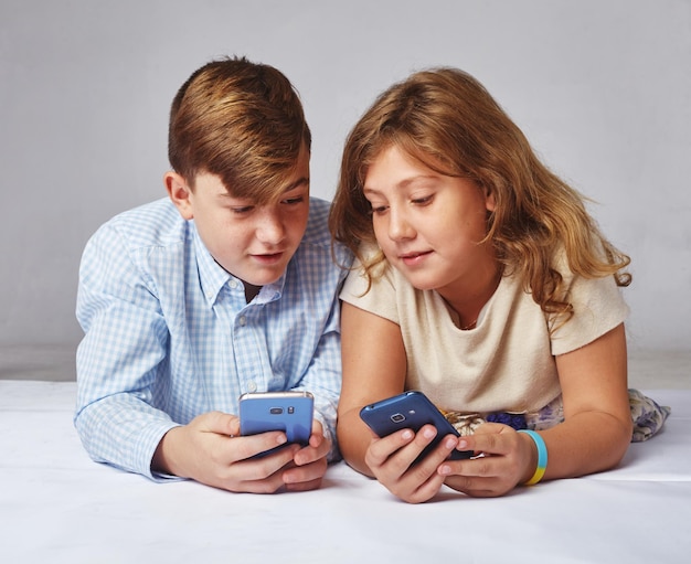 Junges Mädchen und ein Junge, die am Telefon spielen, lächeln und lachen. Kinder lernen neue Technologien