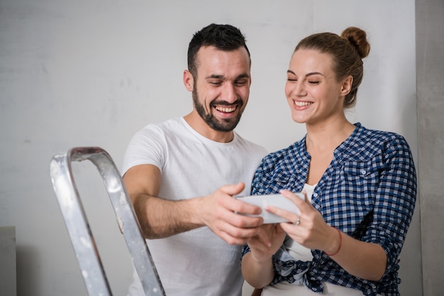 Junges Mädchen und ihr Freund betrachten Fotos auf dem Telefonbildschirm. Sie machen eine Pause von der Renovierung