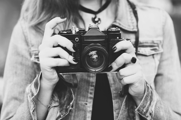 Junges Mädchenfotograf, der in einer Jeansjacke mit einer alten Kamera die Straße entlang geht