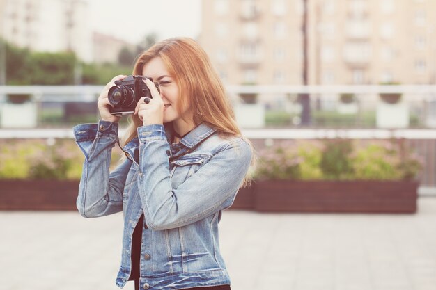 Junges Mädchenfotograf, der in einer Jeansjacke mit einer alten Kamera die Straße entlang geht