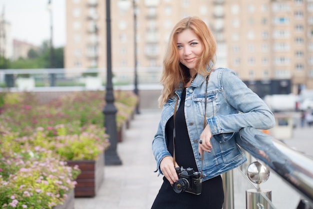 Junges Mädchenfotograf, der in einer Jeansjacke mit einer alten Kamera die Straße entlang geht