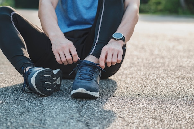 Junges Männchen in Sportbekleidung, das Schnürsenkel im Park im Freien bindet, Sportler-Läufermann, der morgens zum Laufen und Joggen bereit ist. Bewegung, Wellness, gesunder Lebensstil und Trainingskonzept