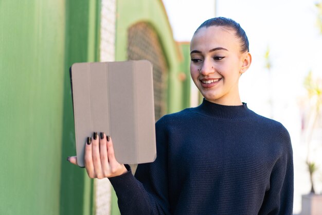 Junges marokkanisches Mädchen, das draußen eine Tablette mit glücklichem Ausdruck hält