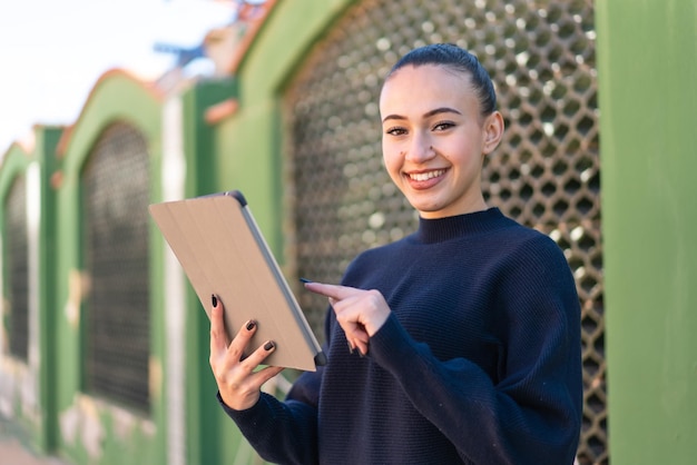 Junges marokkanisches Mädchen im Freien, das den Tablet-Bildschirm mit glücklichem Ausdruck berührt