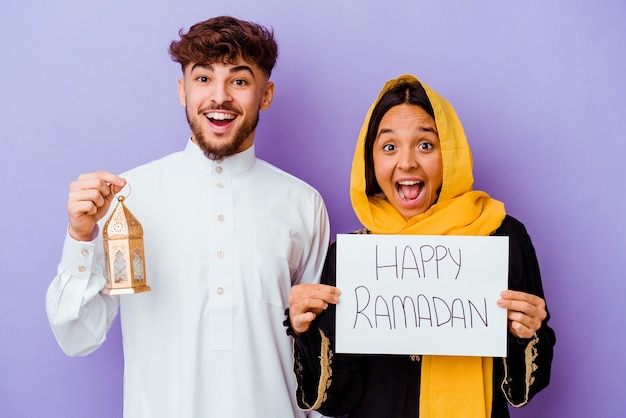 Junges marokkanisches Paar, das ein typisches arabisches Kostüm trägt, das Ramadan lokalisiert auf purpurrotem Hintergrund feiert
