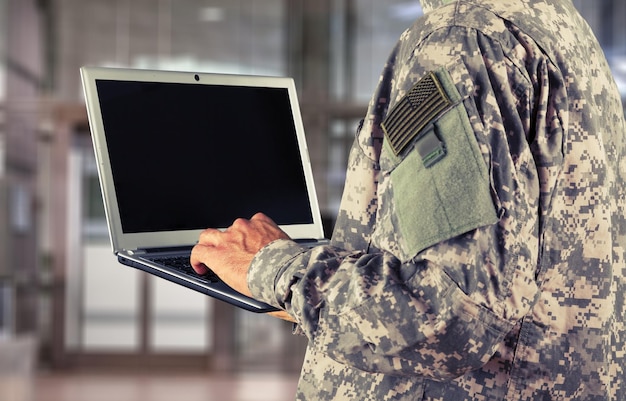 Junges Militärsoldat-Mannporträt mit Laptop auf Hintergrund