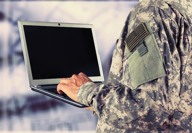 Junges Militärsoldaten-Mannporträt mit Laptop auf Hintergrund