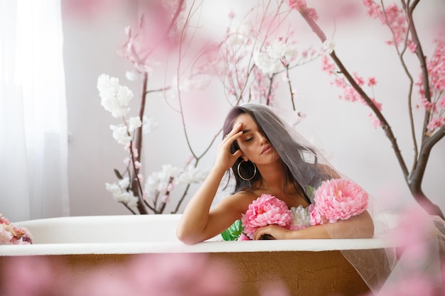 Junges Modell schloss die Augen und saß in einer Badewanne mit Blumenstrauß Hochwertiges Foto