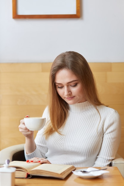 Junges Modell wirft das Sitzen im Café auf und liest interessantes Buch