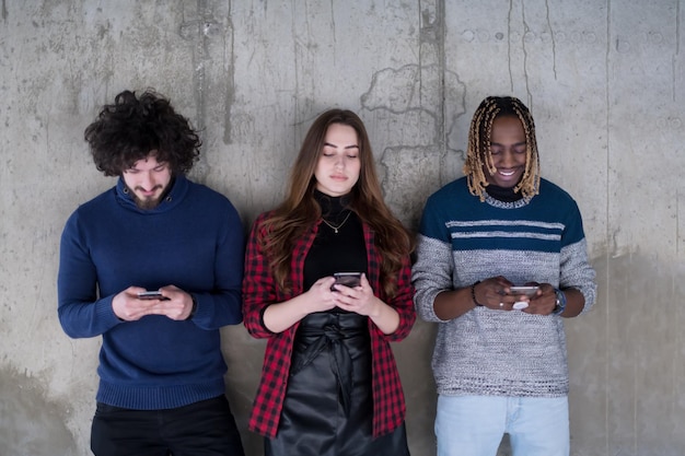 junges multiethnisches erfolgreiches Casual Business Team mit Mobiltelefonen, während es vor einer Betonwand in einem neuen Startup-Büro steht