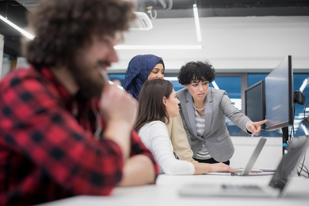 junges multiethnisches Geschäftsteam von Softwareentwicklern, die mit Laptop und Desktop-Computer zusammenarbeiten, während sie Programmiercode in einem modernen Startup-Büro schreiben