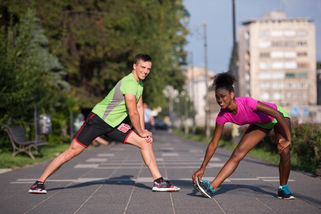 Junges multiethnisches Joggingpaar, das sich vor dem morgendlichen Laufen in der Stadt aufwärmt und dehnt