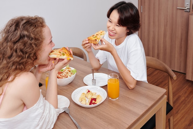 Junges multiethnisches lesbisches Paar, das Pizza zum Abendessen zu Hause isst