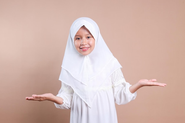 Junges muslimisches Mädchen im Hijab zeigt mit offener Hand eine willkommene Geste auf beige Hintergrund