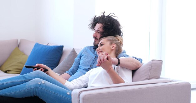 Junges Paar auf dem Sofa, das zusammen in seinem Luxushaus fernsieht
