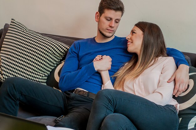 Junges Paar auf dem Sofa in der Liebe. Schönes Paar verbringt einen romantischen Abend. Lächelnde Paar sitzt auf einer Couch beim Betrachten einander