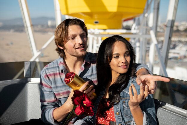 Foto junges paar bei einem date mit dem riesenrad, während es rosen und geschenke in der hand hält