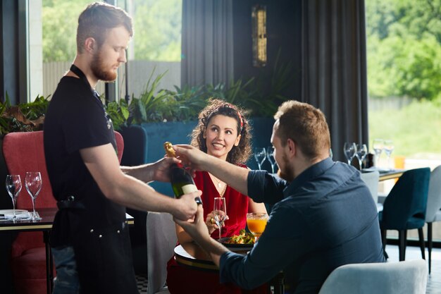 Junges Paar beim Abendessen im Restaurant Kellner brachte eine Flasche Champagner