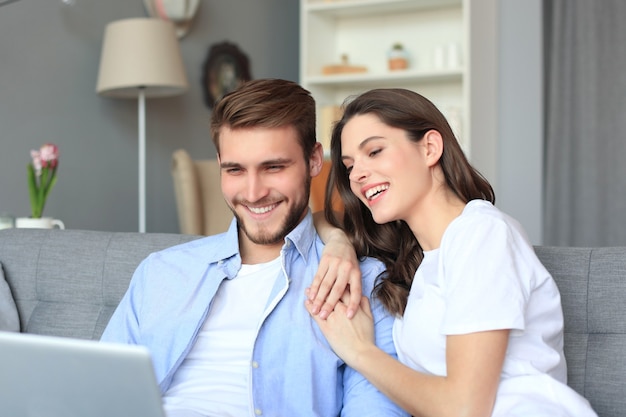 Junges Paar beim Online-Shopping zu Hause mit einem Laptop auf dem Sofa.