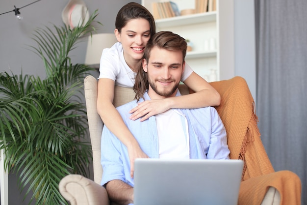 Junges Paar beim Online-Shopping zu Hause mit einem Laptop auf dem Sofa.