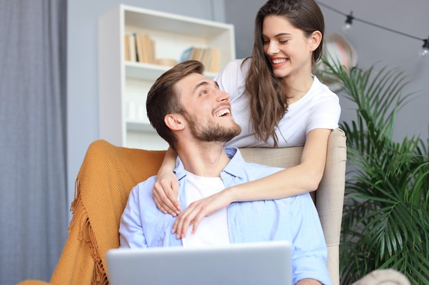 Junges Paar beim Online-Shopping zu Hause mit einem Laptop auf dem Sofa.