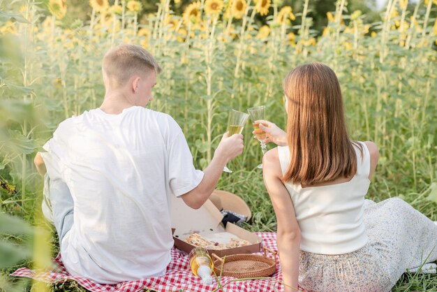 Junges Paar beim Picknick auf Sonnenblumenfeld bei Sonnenuntergang