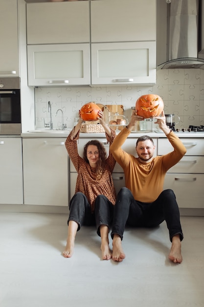 Junges Paar, das auf dem Küchenboden sitzt und Halloween-Kürbisse hält