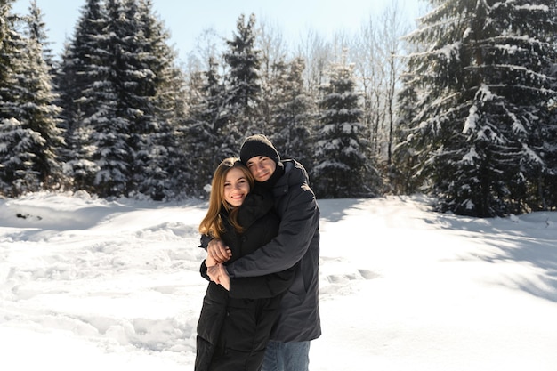 Junges Paar, das auf einem Winterspaziergang in der Nähe des Waldes herumalbert, ein allgemeiner Plan eines verliebten Paares vor dem Hintergrund der Winternatur